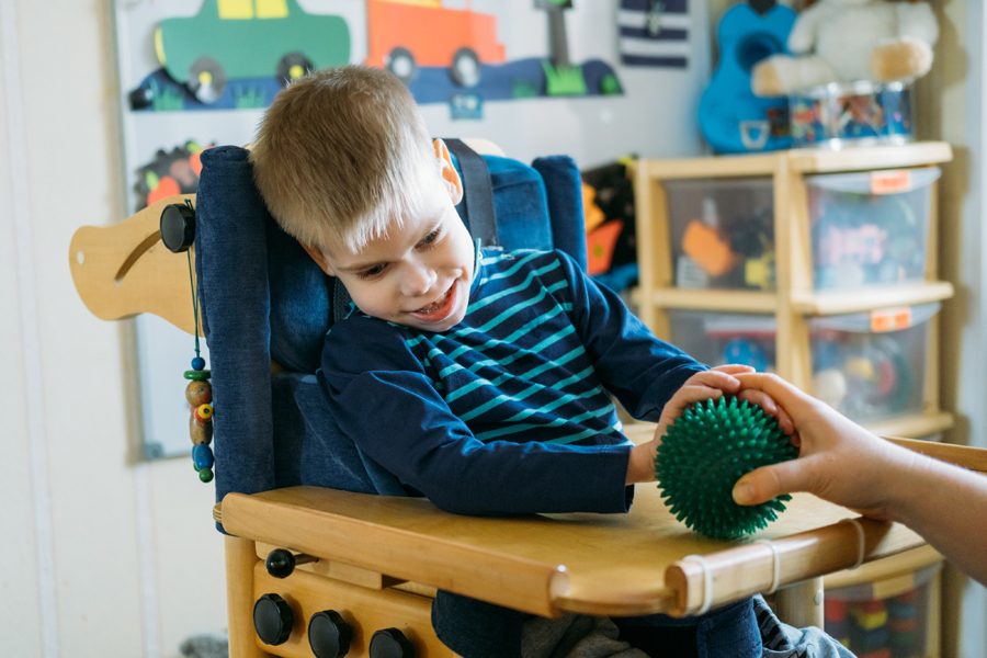 Sensory Activities for kids with disabilities. Preschool Activities for Children with Special Needs. Boy with with Cerebral Palsy in special chair play with mom at home