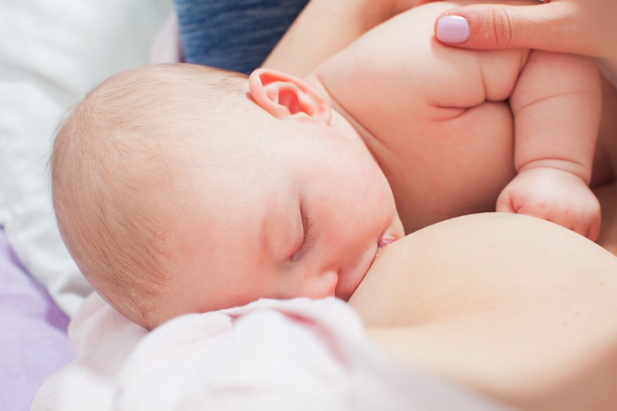 Close portrait of adorable baby sleeping while breastfeeding. Newborn baby nursing with widely open mouth. Breastfeeding support techniques, skin to skin contact