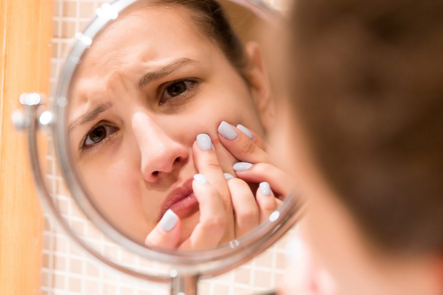 Young girl squeezes pimple on the fer face in front of a bathroom mirror. Beauty skincare and wellness morning concept.