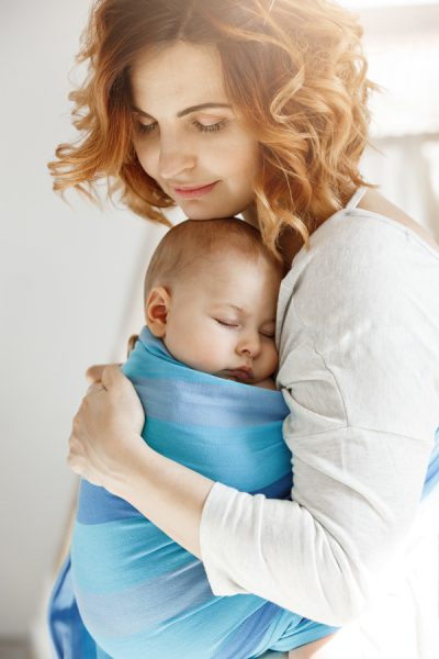 Portrait of young mother and newborn son sleeping on mother chest in baby sling. Family happiness vibes. Family concept
