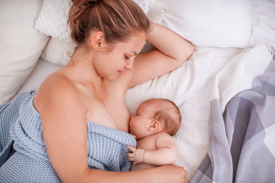 Happy young woman breastfeeding and hugging baby. mom breastfeeding newborn child lying on bed. Lactation newborn concept. Baby eating milk before sleeping. Mother feed her month son with breast milk