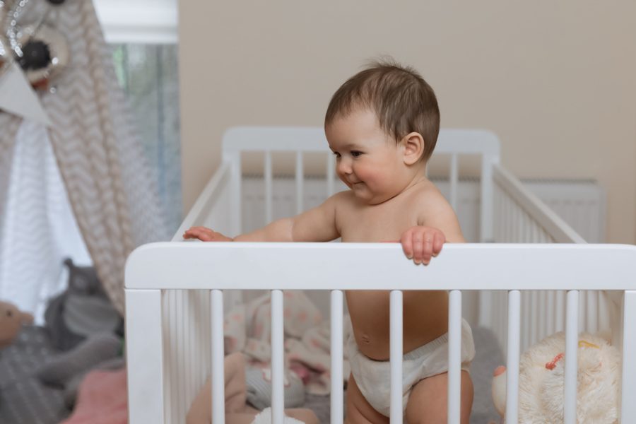 Baby girl in a diaper playing in the crib. Very funny face expression.