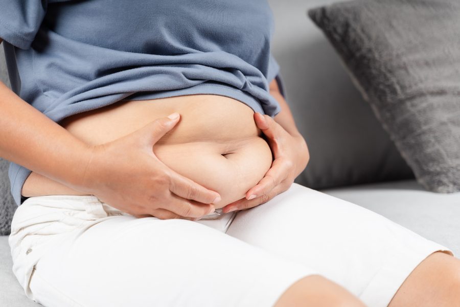 Close up of chubby woman holding her belly fat on the sofa. Diet lifestyle to reduce belly and shape up healthy abdominal muscle concept.