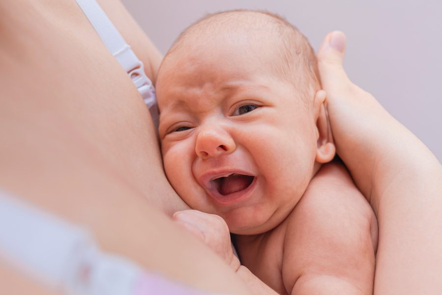 Baby crying on mother's breast close-up