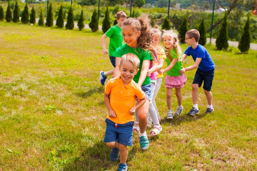 Children playing snake game, holds each other and run on the lawn