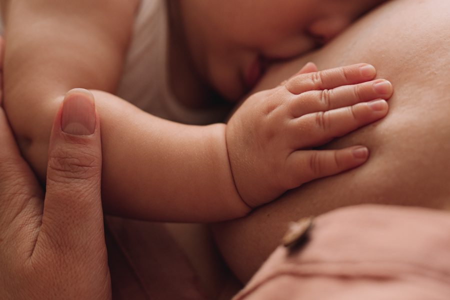 Close-up of baby hand on mother's breast. Mother breastfeeding baby. Concept of motherhood and breastfeeding.