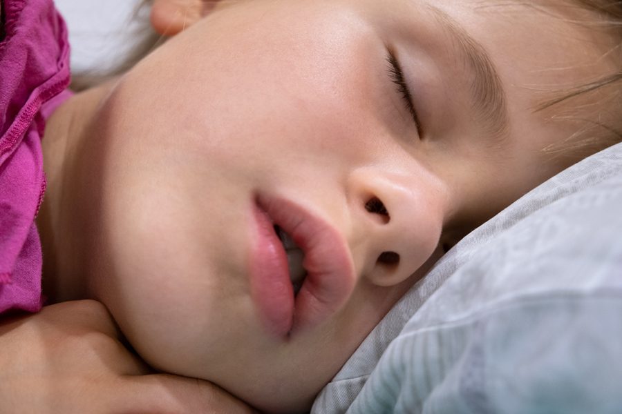 Close up of a face of pretty little child girl with slightly open mouth and scattered around hair sleeping in bed at home.