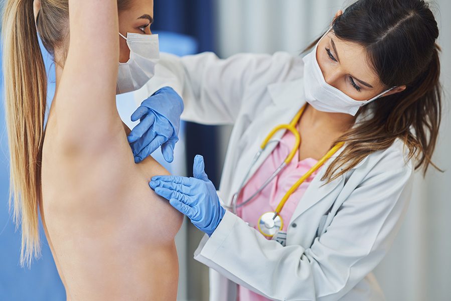 Picture of doctor in mask checking up breast to her patient