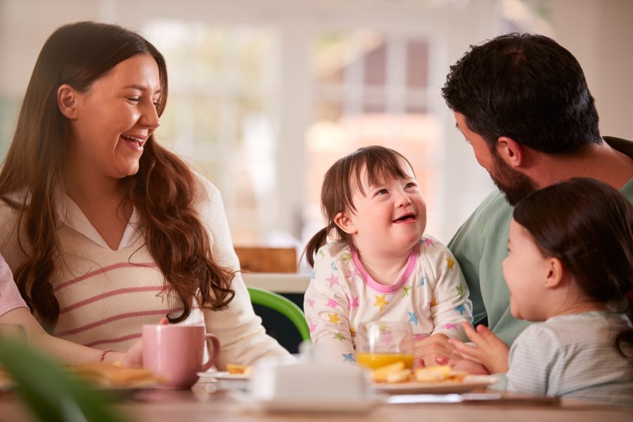 Family With Down Syndrome Daughter Sitting Around Table At Home Eating Breakfast