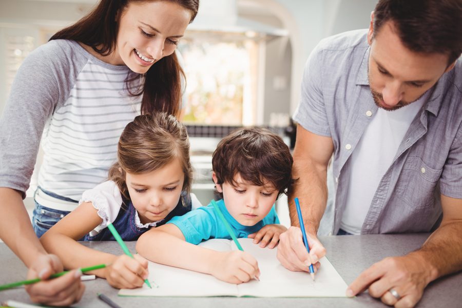 Family writing in book while standing at table in house