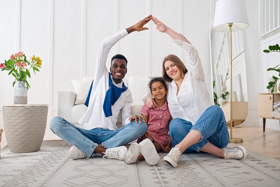 Happy family sitting on the floor in living room. Mother, father and their daughter poses at home together, good relationship