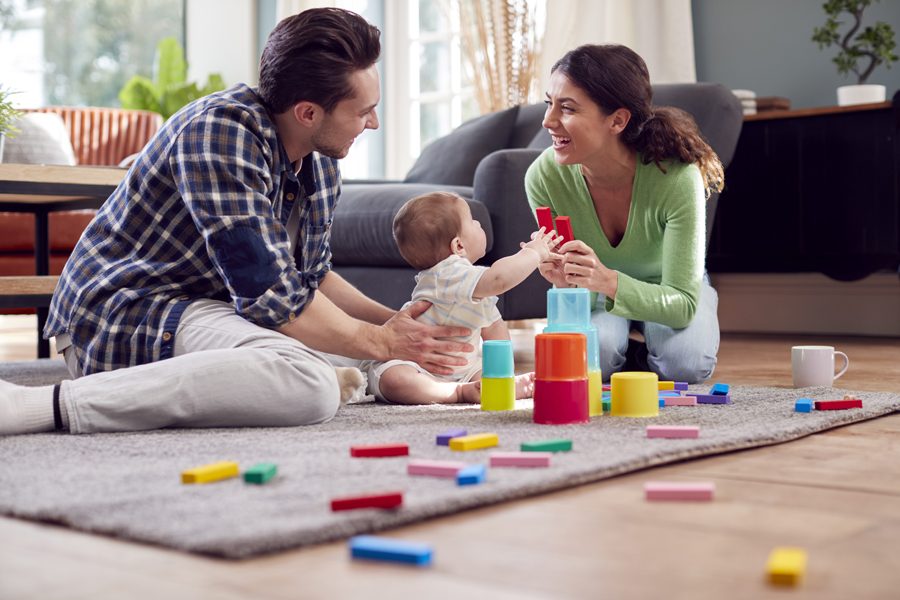 Transgender Family With Baby Playing Game With Colourful Toys In Lounge At Home