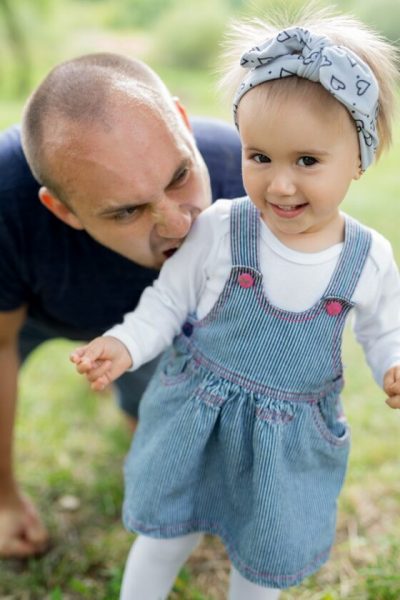 The father plays with his daughter and wants to bite her for fun. A cute girl has fun with her dad. Father's Day.