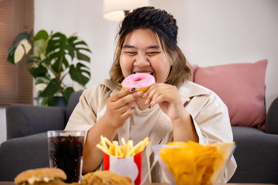 Happy Asian fat woman enjoy eating delicious sweet donut and fast food on living room.