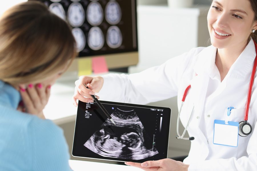 Woman obstetrician gynecologist showing patient photograph of ultrasound examination of fetus on digital tablet. In vitro fertilization concept