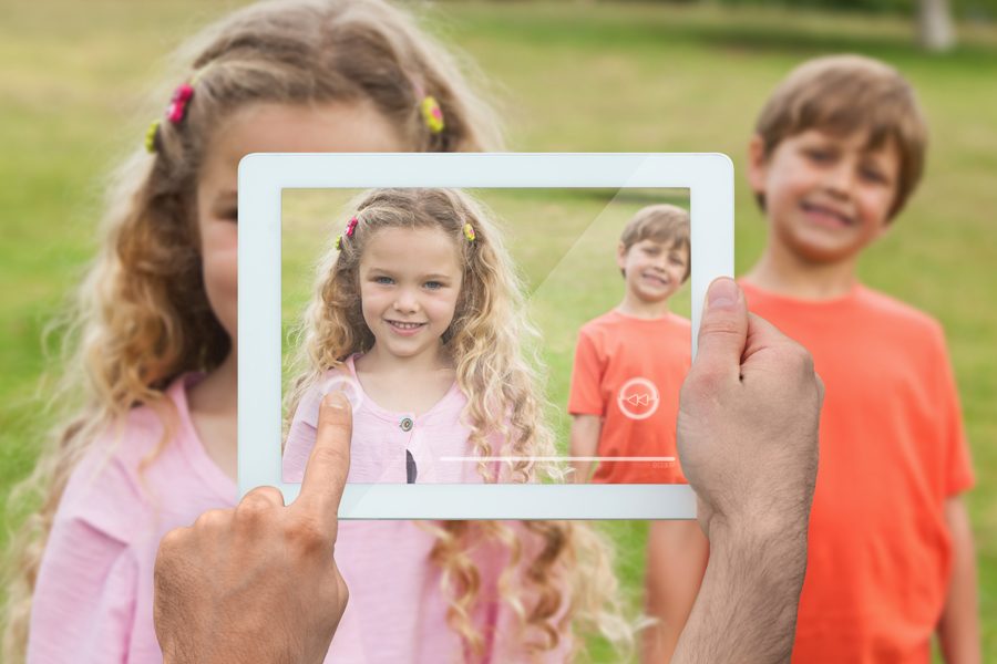 Hand holding tablet pc showing cute siblings smiling at camera