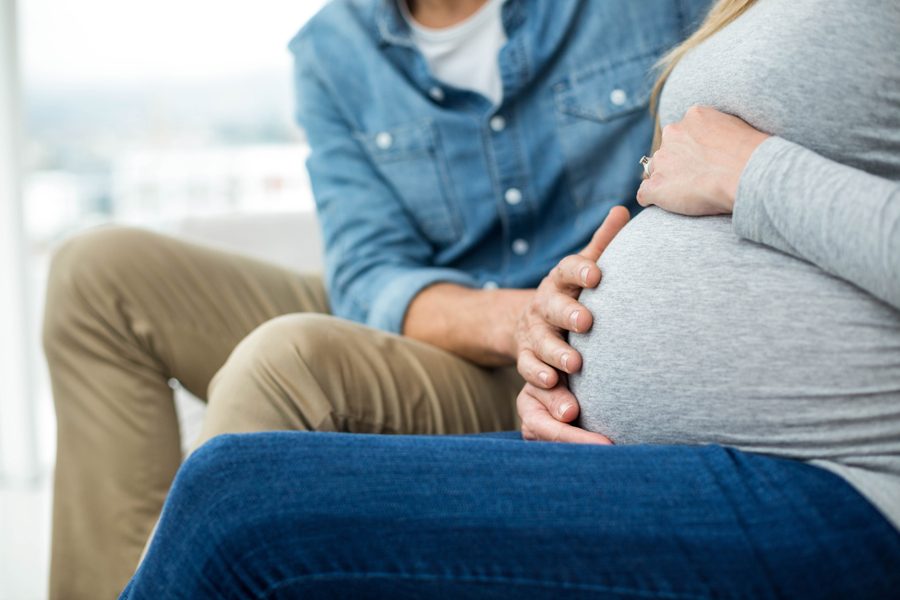 Man sitting on sofa and holding pregnant womans stomach