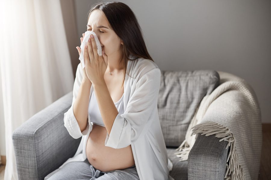 Young pregnant woman suffering from flu. Coughing and using a tissue. Keeping healthy pregnancy is hard.