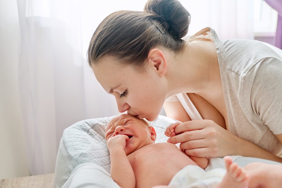 Young mom kissing crying newborn baby son. Infancy, motherhood, parenthood, love, family concept