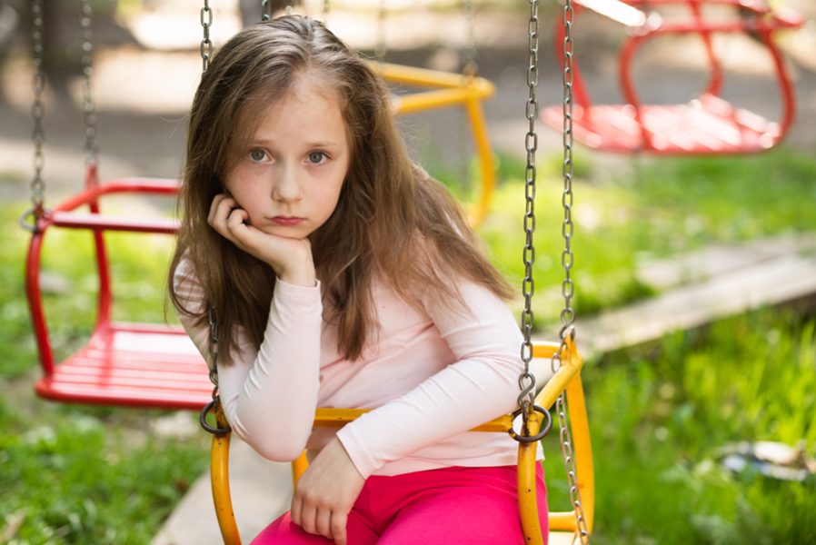 Little child swinging. Girl with a face expressing boredom and anticipation. Little girl walk in adventure park. Child playing on outdoor playground