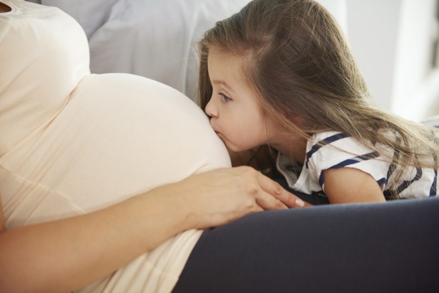 Little girl kissing her future sibling