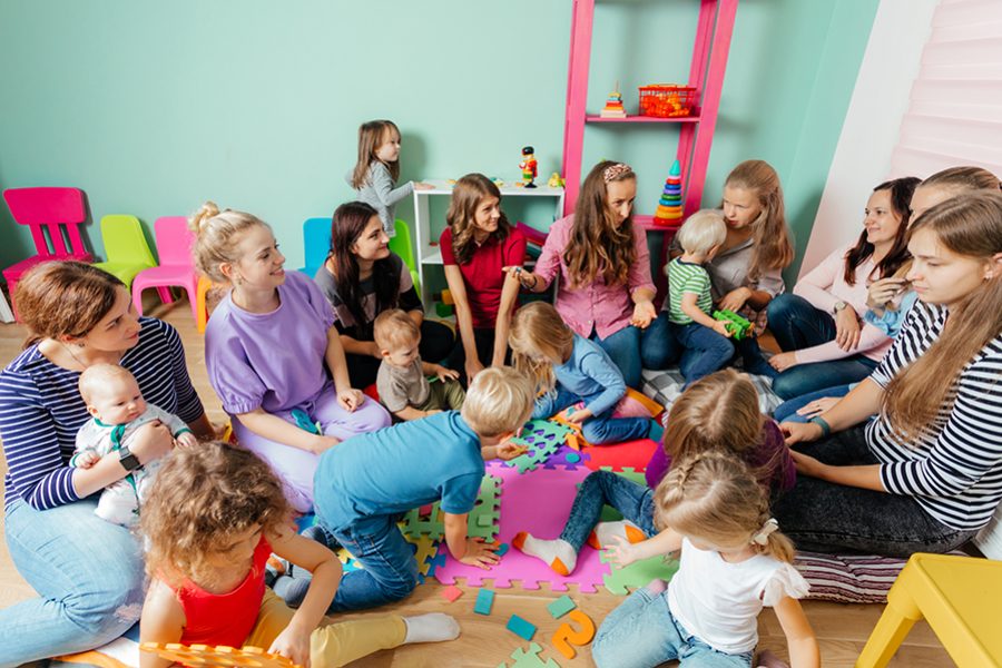 Group of preschoolers with their mothers sitting on a floor at the nursery. Happy children's communication supported by mothers. Adaptation period at the kindergarten.
