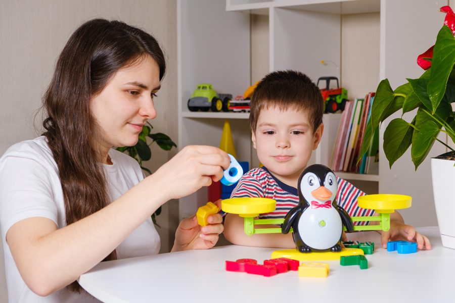 Mom and son play with numbers, weigh a penguin on a toy scale