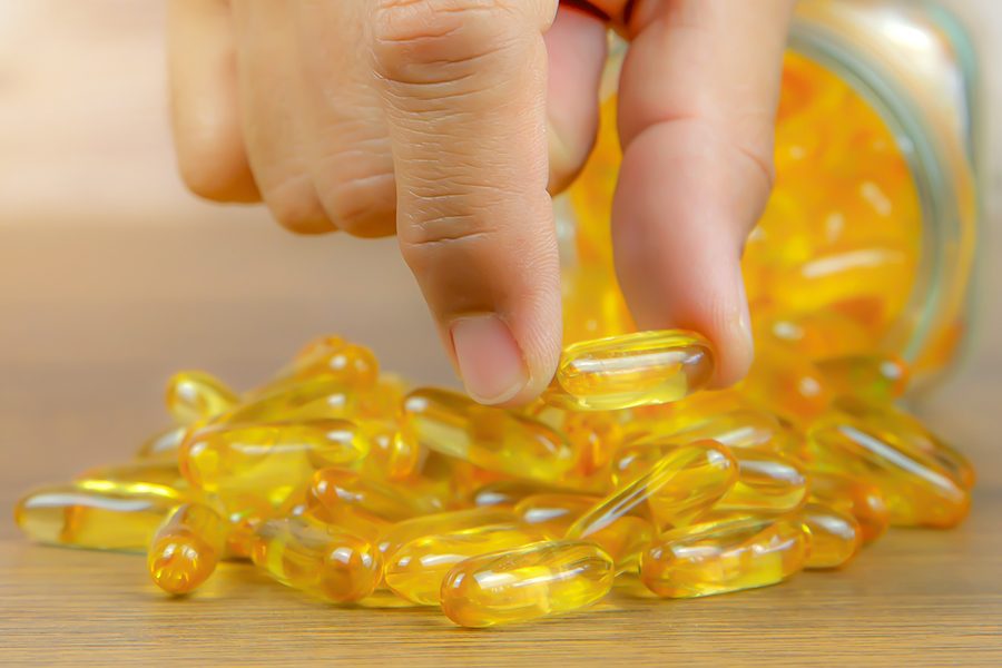 Hand choose a cod liver oil  capsule from a pile of cod liver oil or fish oil dietary supplement for health-care concepts.