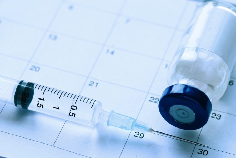 Medical syringe and medication vial on calendar background with copy space. Vaccination schedule healthcare concept