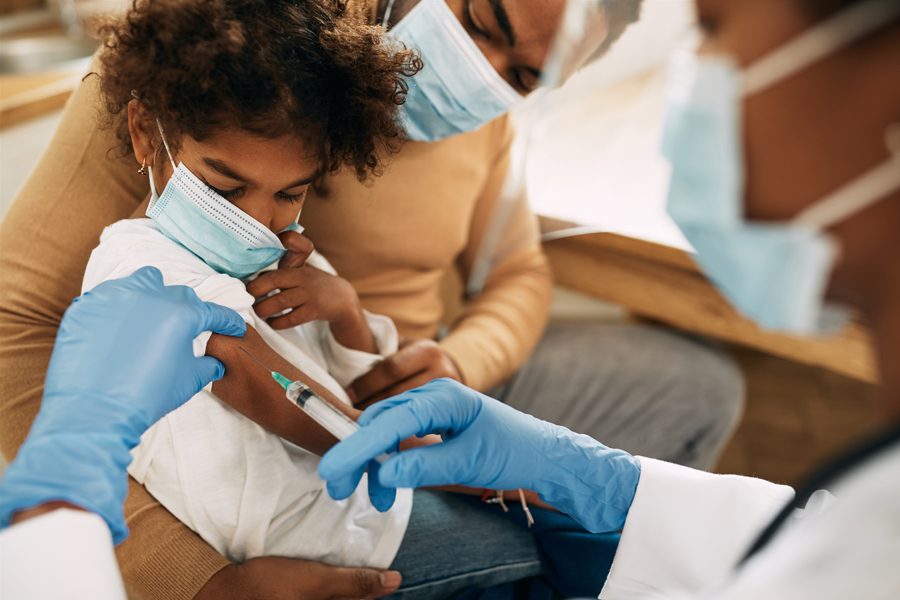 Black little girl getting vaccinated at doctor's office due to virus pandemic.