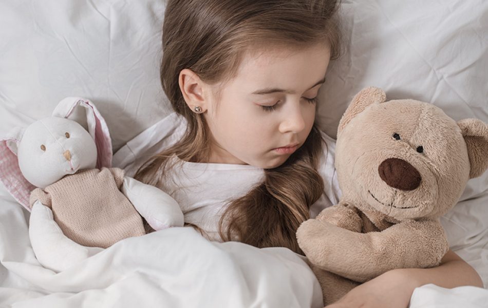 Cute little girl in a white bed sleeping with a soft toy . The concept of children's sleep and development .