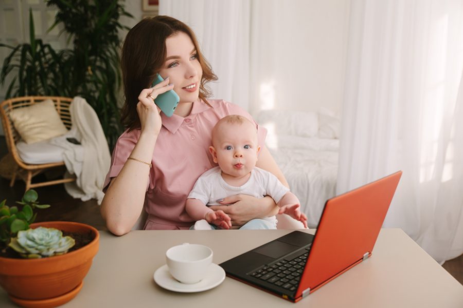 Mother and baby in home office with laptop and telephone.