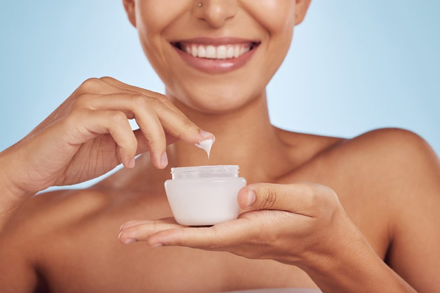 Beauty, lotion and woman with skincare product for cosmetic hydration isolated in a studio blue background. Cream, moisturizer and happy female person with a jar of dermatology creme for healthy skin.