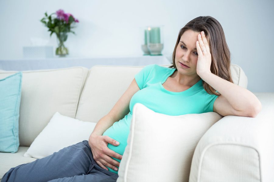 Pregnant woman with headache sitting on sofa