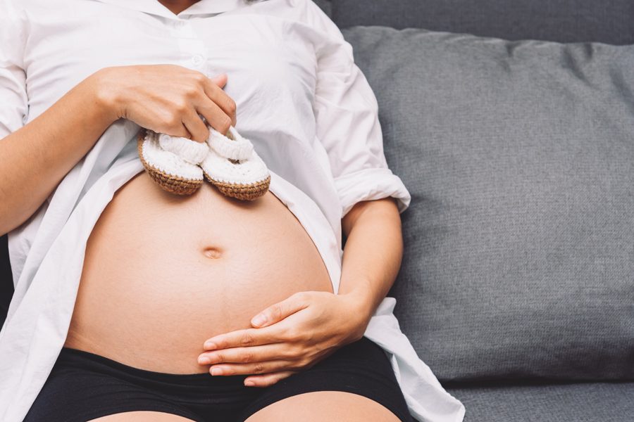 Pregnancy woman holding pair of shoes on her belly, preparing baby product for her baby.