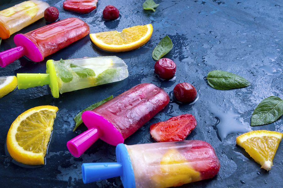 Multicolored bright fruit popsicle with strawberry, cherry, lemon, orange, lemon and mint aroma and fresh fruit on a dark blue background.