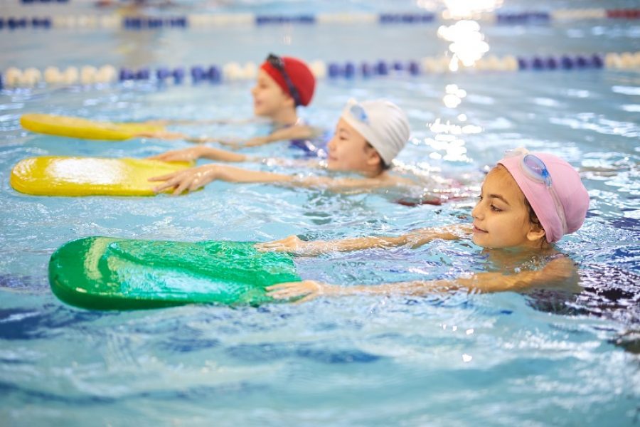 Young girl in swimwear and swimming cap using boards in the swimming pool,  they learning to swim