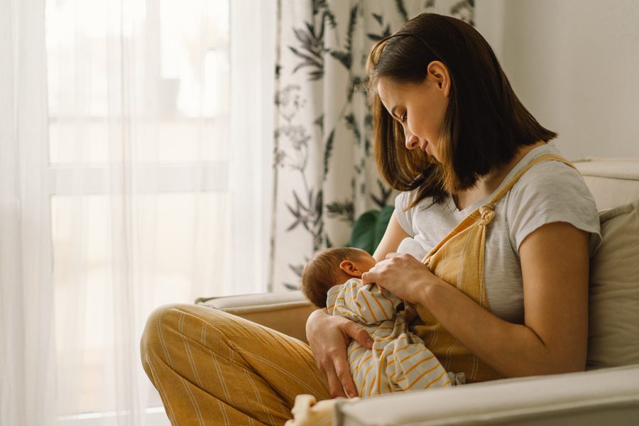 Newborn baby boy sucking milk from mothers breast. Portrait of mom and breastfeeding baby. Concept of healthy and natural baby breastfeeding nutrition.