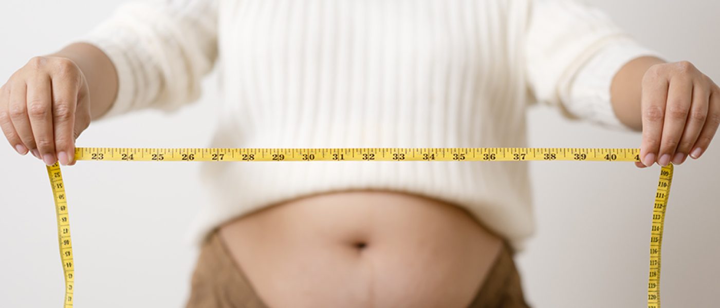An obesity using measuring tape to show the real size. Chubby fat woman using measure tape at belly. Real size woman after gave birth to baby, real skin with wrinkles and scars.