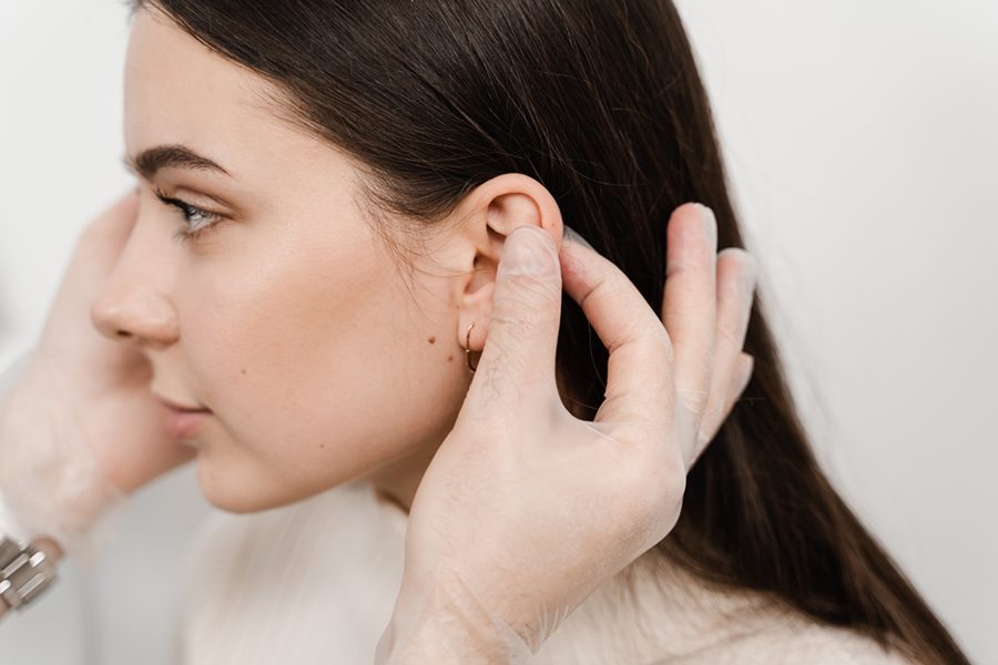 Otoplasty ear surgery. Surgeon doctor examines girl ears before otoplasty cosmetic surgery. Otoplasty surgical reshaping of pinna and ear