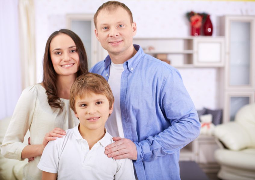 Portrait of happy lad and his parents looking at camera at home