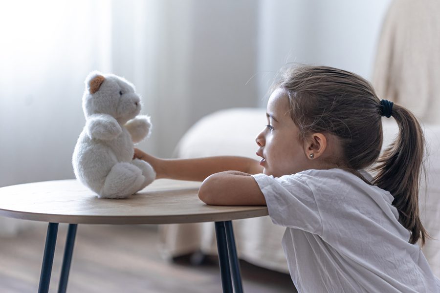 Portrait of a little girl with a teddy bear on a blurred background in the interior of the room.