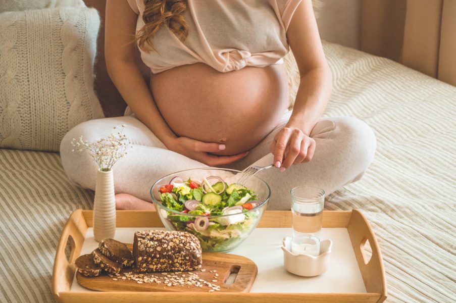 Pregnancy and healthy organic nutrition. Pregnant woman enjoying fresh vegetable salad in bed, free space. Concept of expectation and health.