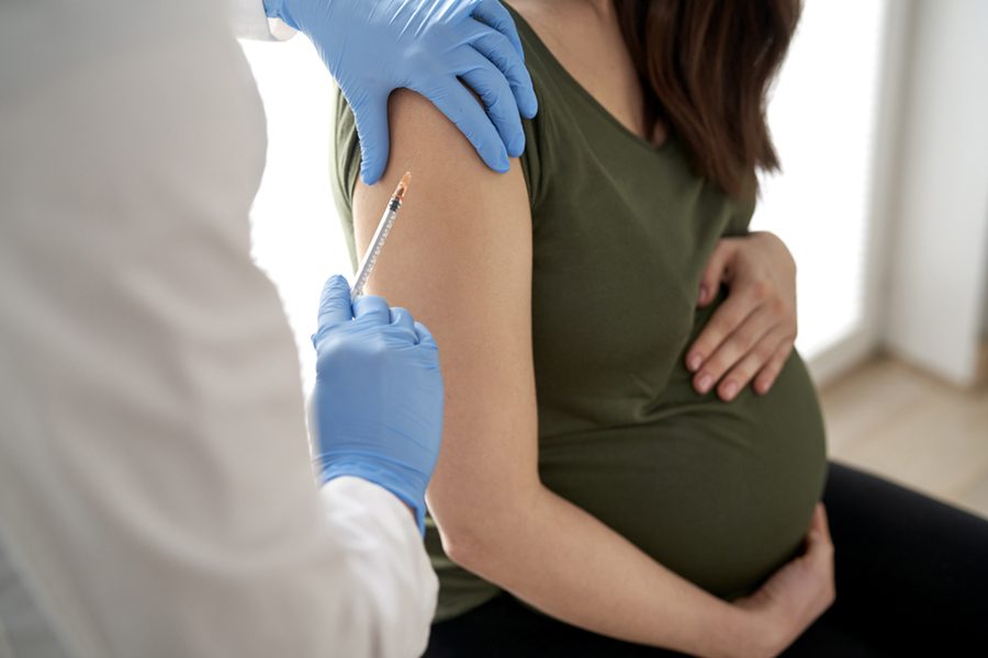 Pregnant caucasian woman sitting with protective mask after vaccination