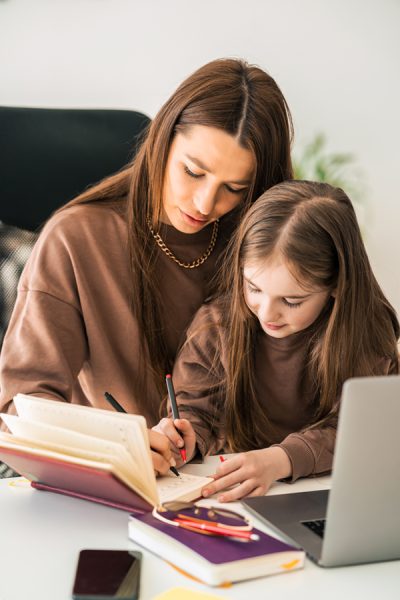 Mother and daughter are doing homework at the laptop. Little schoolgirl at the distance learning at home