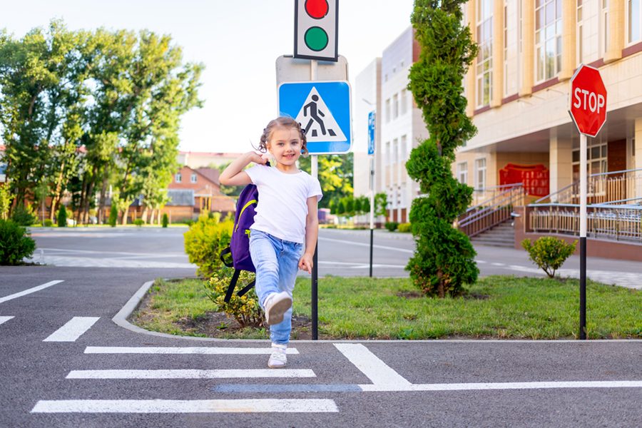 a schoolgirl girl crosses the road on a zebra near the road sign pedestrian crossing going to school with a backpack the concept of traffic rules