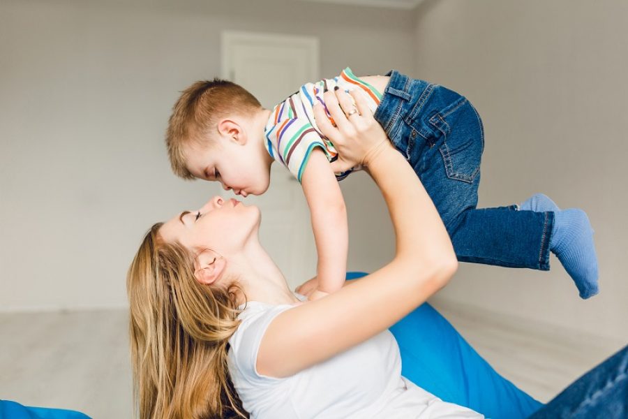 Studio shot of a mother playing with her child. Mom holds boy in her arms. Mom wears white t-shirt, and boy is dressed into jeans and white shirt. They are having fun.