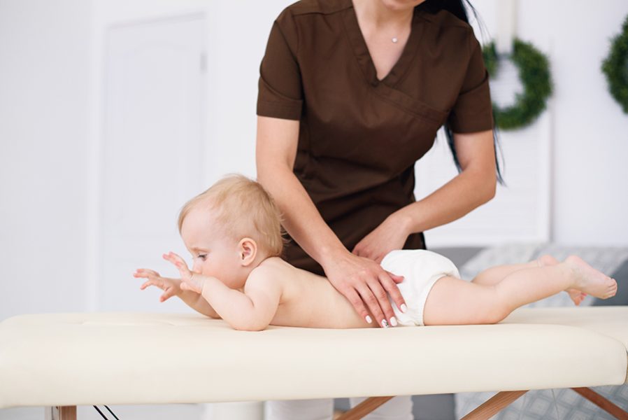 Therapist makes massage to a little baby at modern cozy room. Health care and medical concept.