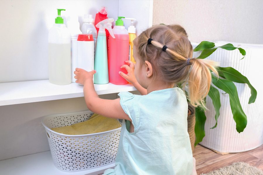 Toddler touches bottles of household chemicals, household cleaning products. Dangerous situation