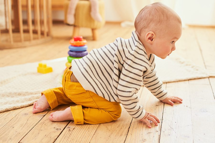 Portrait of cheerful healthy handsome little boy crawling on the wooden floor of the children's room. Happy healthy child having fun with colorful wooden toys at home. Early development for children.